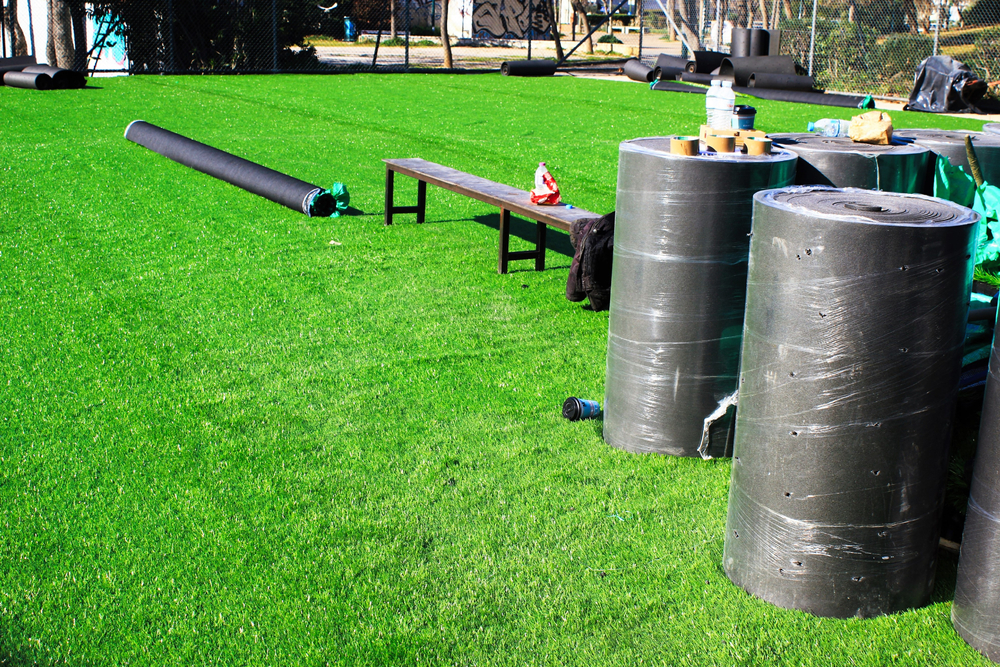 Artificial turf installation in progress in a Vancouver yard with turf rolls, tools, and a prepared green surface