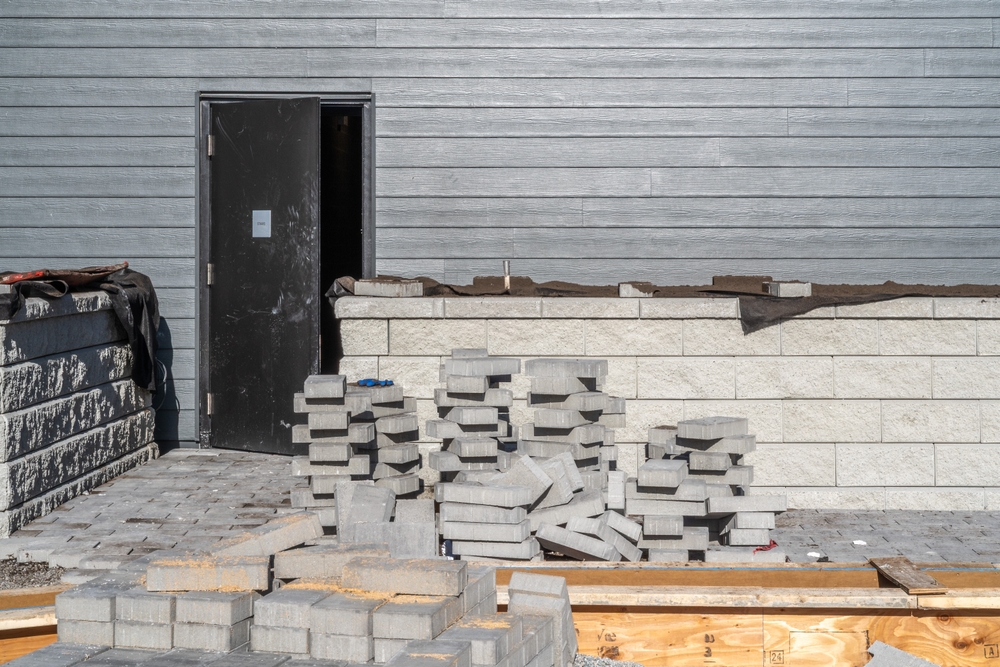 Hardscape construction in progress with stacked concrete pavers and a partially built retaining wall