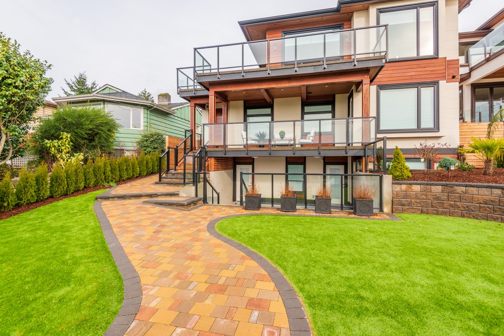 Modern Burnaby backyard with a curved paver walkway, manicured lawn, retaining wall, and tiered glass-railing decks