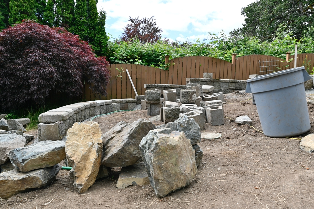 Backyard retaining wall and stonework construction in progress with stacked stone, boulders, and a Japanese maple
