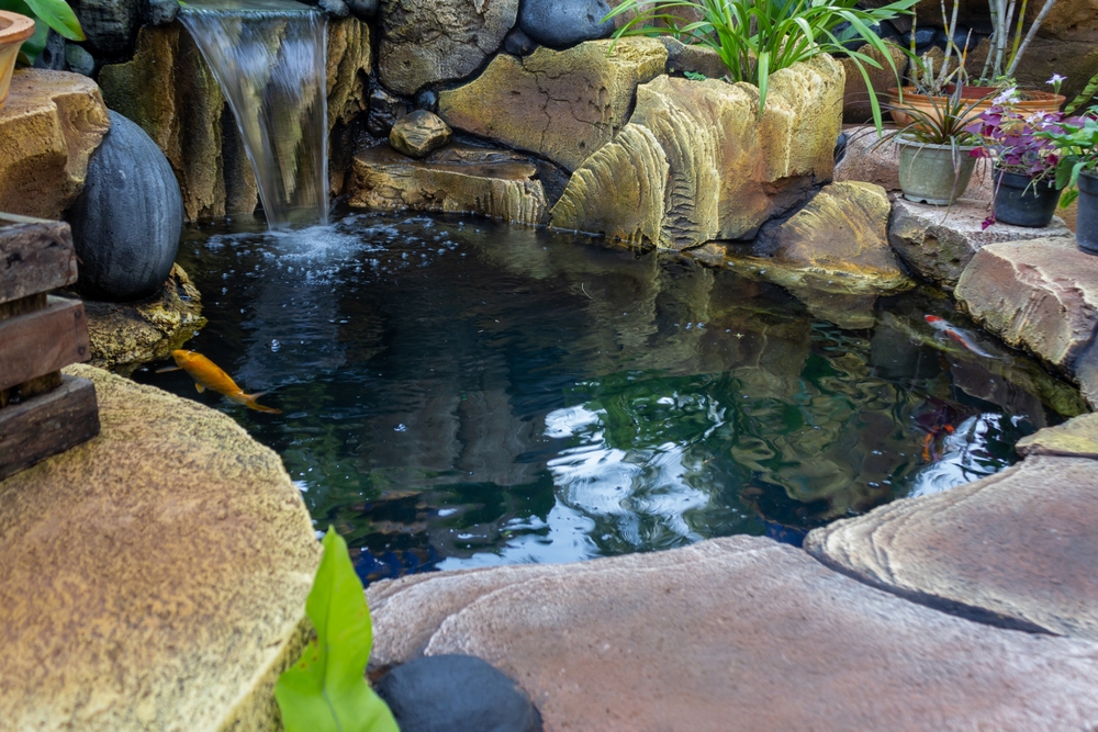 Backyard decorative koi pond with a rock waterfall, stone edging, and potted plants