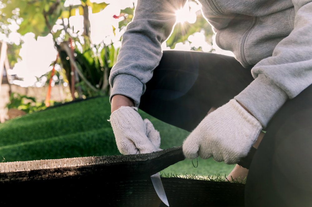 Installer wearing work gloves trimming and securing the edge of newly laid artificial turf