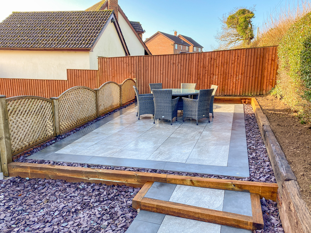Finished outdoor porcelain tile patio and walkway with an artificial turf strip in a landscaped backyard