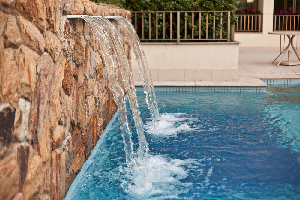 Two arching water spouts pouring from a natural stone wall into a tiled swimming pool