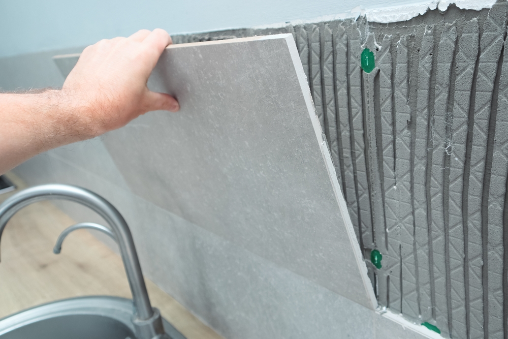 Hand placing a large grey porcelain tile onto a notched thin-set adhesive bed