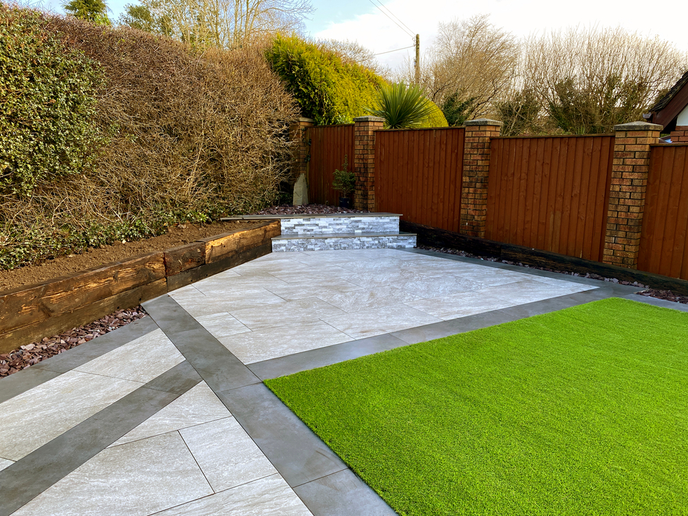 Completed porcelain tile patio with an outdoor dining set bordered by timber edging and gravel beds