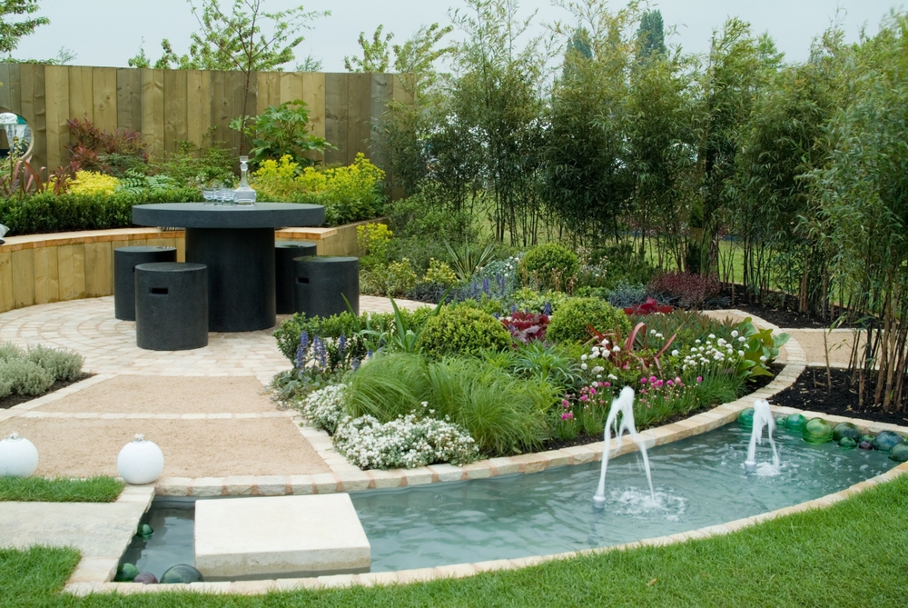 Landscaped backyard with a curved water channel and bubbling fountain jets beside a paved seating area